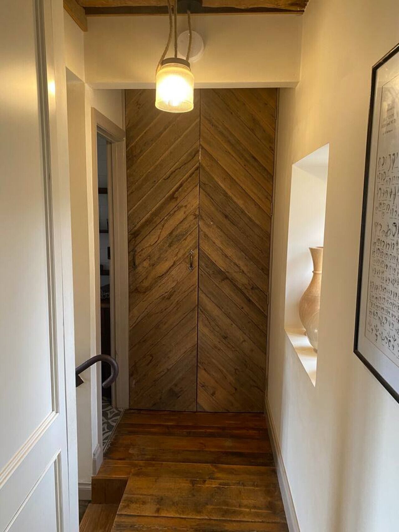 A hallway with a wooden herringbone floor and a door with a similar pattern.