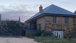 Una casa de piedra con techo de metal, patio cercado y un cobertizo pequeño.