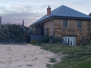 A stone house with a metal roof, a fenced yard, and a small shed. - Granny`s Cottage at Yandoit (Yandoit)