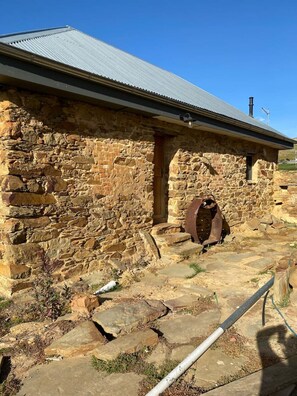 Un edificio de piedra con techo de metal, puerta de madera y reja metálica.