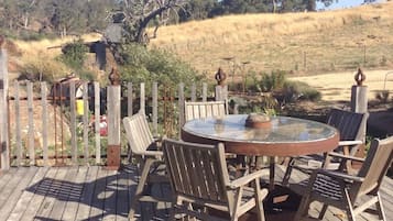 Een houten terras buiten met een ronde glazen tafel en stoelen, omringd door een houten hek.