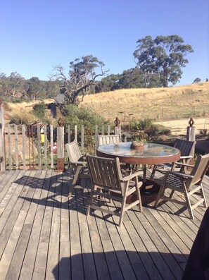 An outdoor wooden deck with a round glass table and chairs, surrounded by a wooden fence. - Granny`s Cottage at Yandoit (Yandoit)