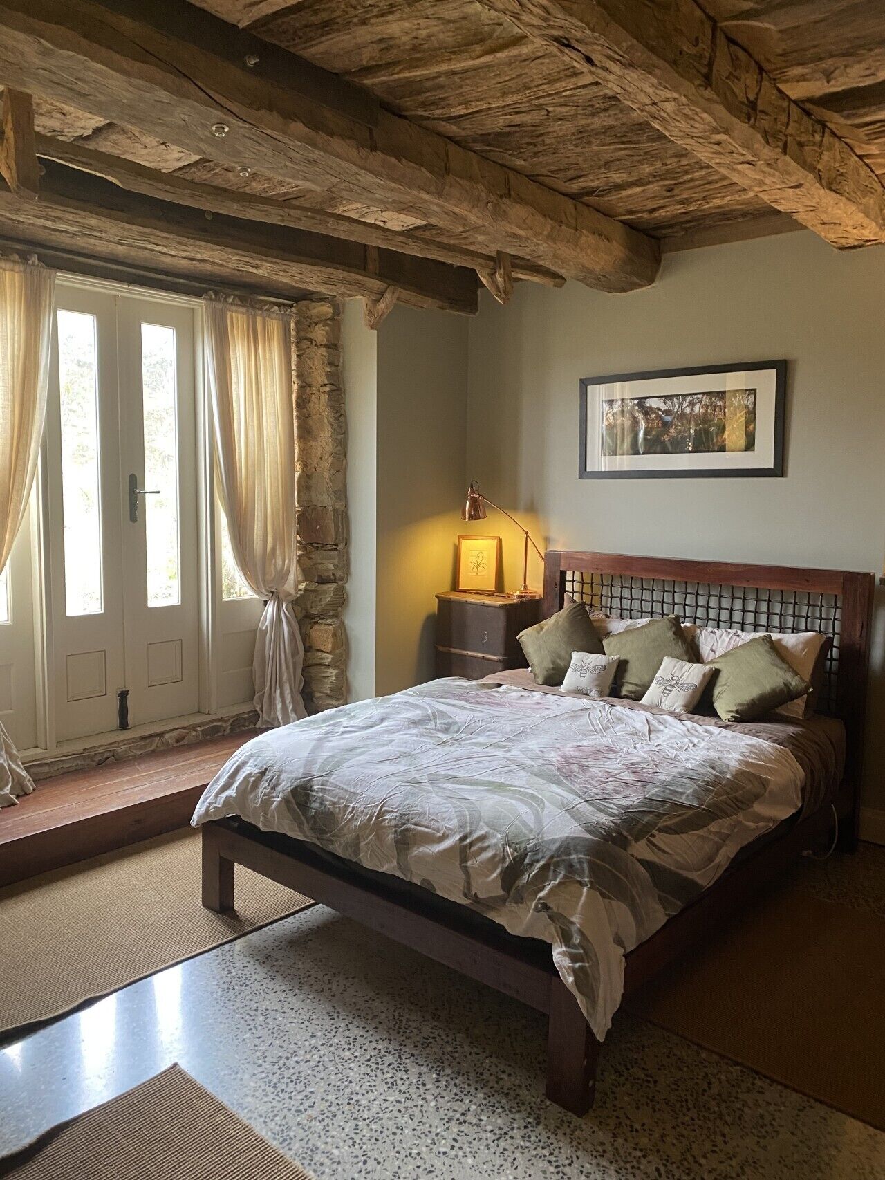 A bedroom with a wooden bed, stone walls, a stone bench, and a framed picture on the wall.