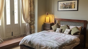 Un dormitorio con una cama de madera, paredes de piedra, un banco de piedra y un cuadro en la pared.