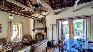 Una sala rústica con chimenea, sofá de cuero, mesa de comedor y vistas al exterior.