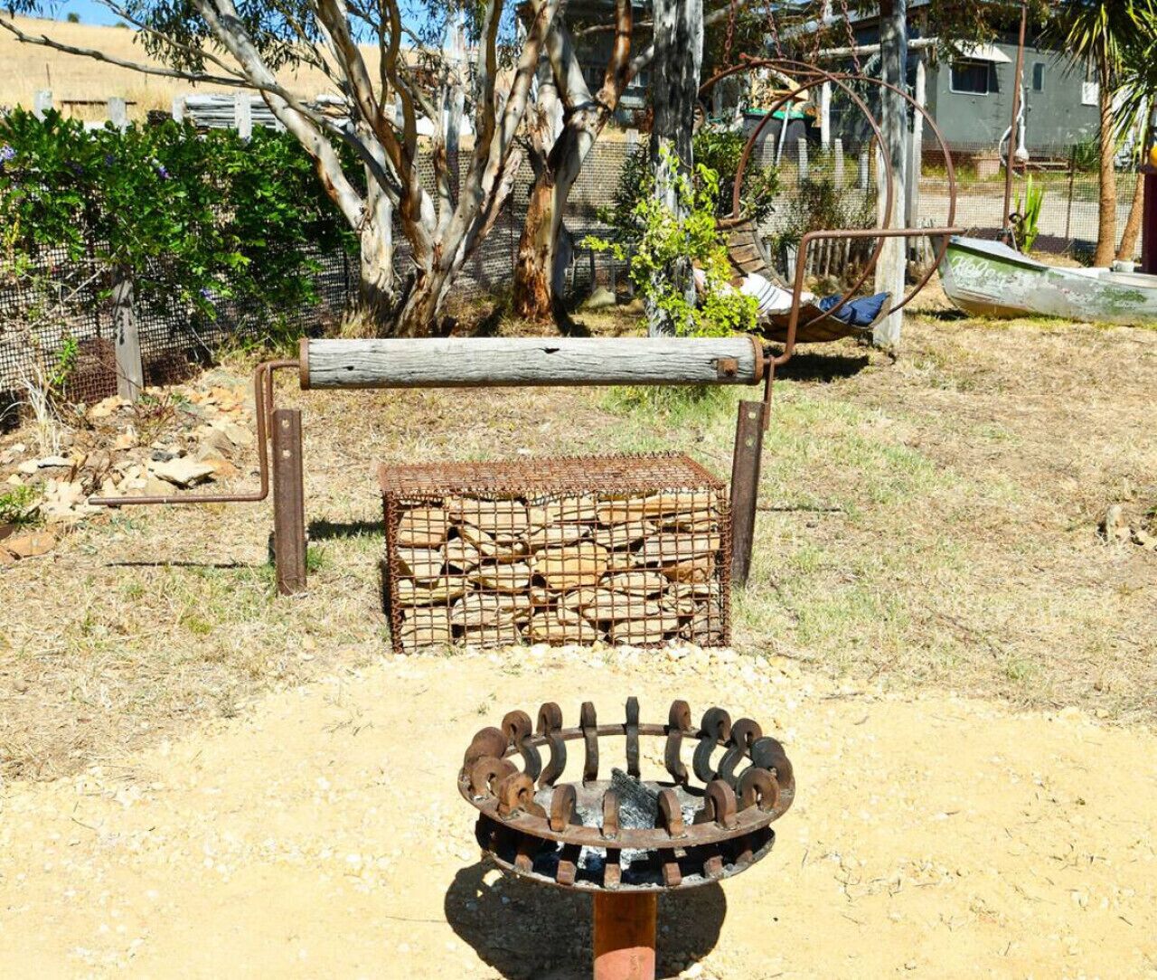 A metal grill with a wooden post in a dry, grassy area with a fence and trees in the background.