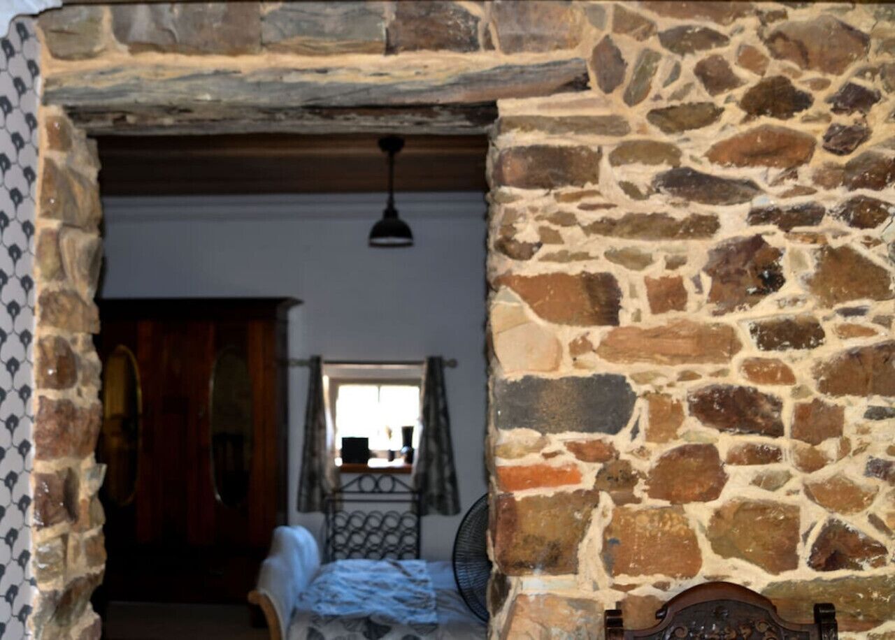 A stone-walled room with a bed, a chair, and a window.