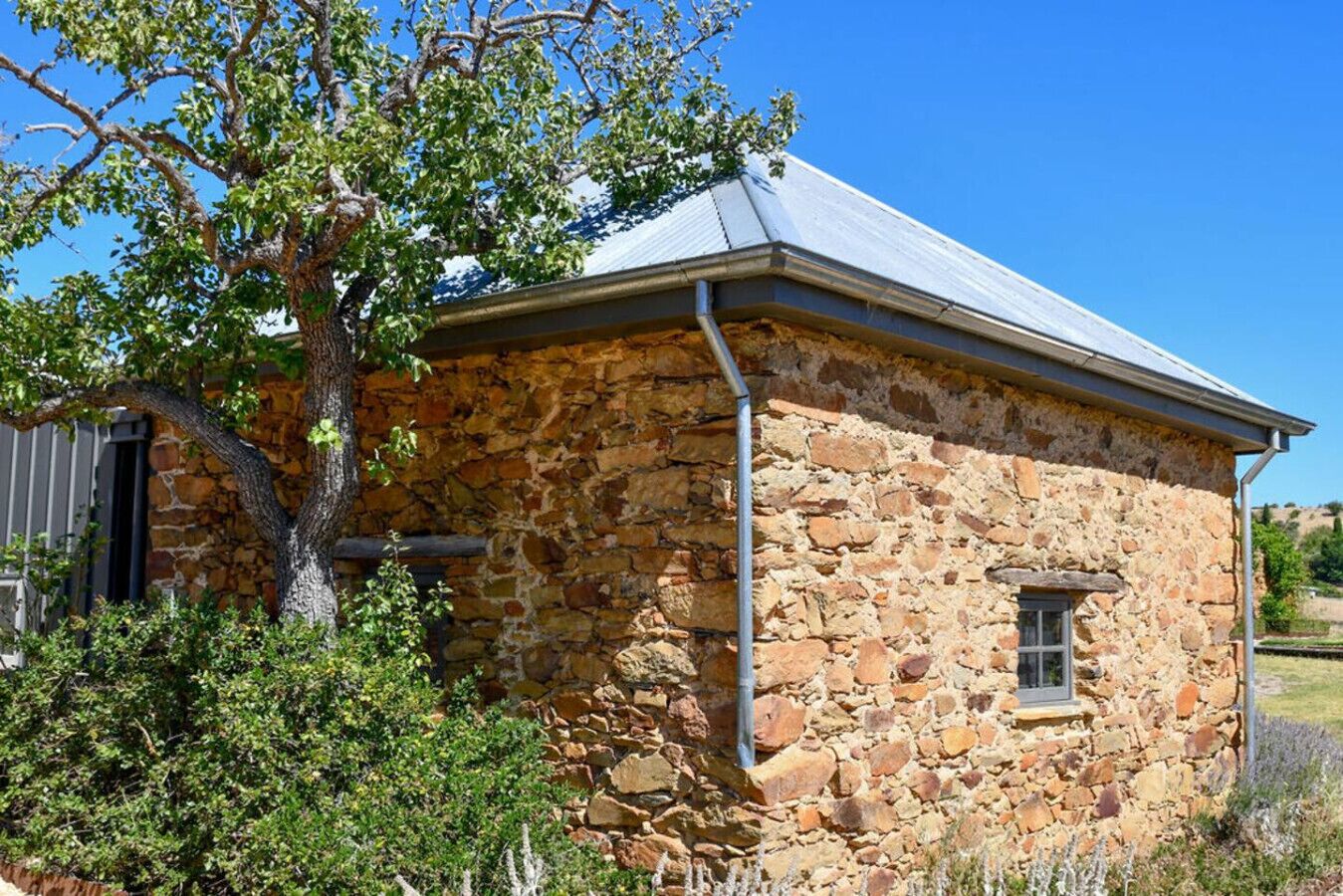 A stone building with a metal roof, a window, and a tree in front.