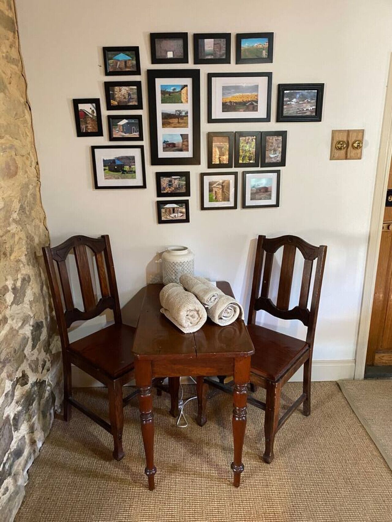 A dining area with a wooden table and chairs, a rug, and a wall decorated with framed pictures.