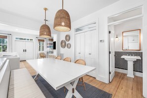 Una cocina moderna con encimera blanca, dos lámparas colgantes de mimbre y una zona de comedor con mesa y sillas de mimbre.