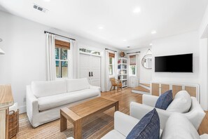 Ein modernes Wohnzimmer mit einem weißen Sofa, einem Holztisch und einem an der Wand befestigten Fernseher.