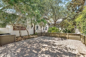 A paved courtyard with a wooden fence, trees, and a building in the background. - Amos Cottage in Rosemary Beach - bikes, pools, and much more! (Inlet Beach)