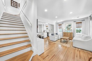 A modern interior with a wooden staircase, a dining area, and a living room with white furniture. - Amos Cottage in Rosemary Beach - bikes, pools, and much more! (Inlet Beach)