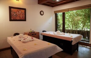 A room with two massage tables, a clock, a painting, and a view of greenery outside. - Gokulam Grand Resort and Spa Kumarakom (Kottayam)