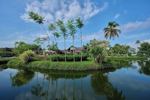 A resort with a water body in the foreground, surrounded by palm trees and a building with a brown roof. - Gokulam Grand Resort and Spa Kumarakom (Kottayam)
