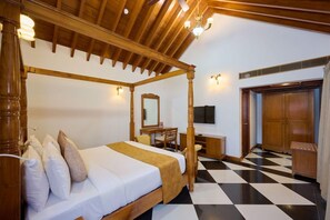 A four-poster bed with a wooden headboard, a desk with a chair, a television, and a wardrobe in a room with a checkered floor. - Gokulam Grand Resort and Spa Kumarakom (Kottayam)