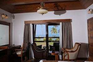 A room with a wooden ceiling, a chandelier, a desk with a chair, a sofa, and a view of palm trees through large windows. - Gokulam Grand Resort and Spa Kumarakom (Kottayam)