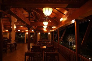 An indoor dining area with wooden beams and tables, illuminated by hanging lamps. - Gokulam Grand Resort and Spa Kumarakom (Kottayam)