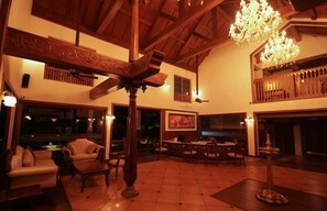 A spacious interior with a high ceiling, wooden beams, and a chandelier. There is a dining area with a table and chairs, and a seating area with sofas. - Gokulam Grand Resort and Spa Kumarakom (Kottayam)