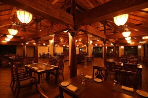 A restaurant with wooden beams and chandeliers, tables set with plates and glasses, and a warm ambiance. - Gokulam Grand Resort and Spa Kumarakom (Kottayam)
