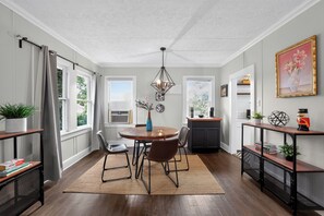A dining area with a round table, chairs, a hanging light fixture, and a view of the outdoors through large windows. - Cozy Private 1-BR Upper Unit with Kitchen - 5111B (Tampa)