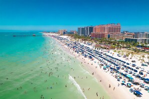 A beach with numerous umbrellas and people, a pier extending into the water, and several high-rise buildings in the background. - Cozy Private 1-BR Upper Unit with Kitchen - 5111B (Tampa)