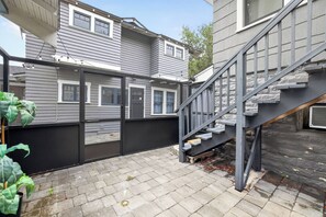 A residential backyard with a wooden staircase leading to a deck, a metal fence, and a house with multiple windows. - Cozy Private 1-BR Upper Unit with Kitchen - 5111B (Tampa)