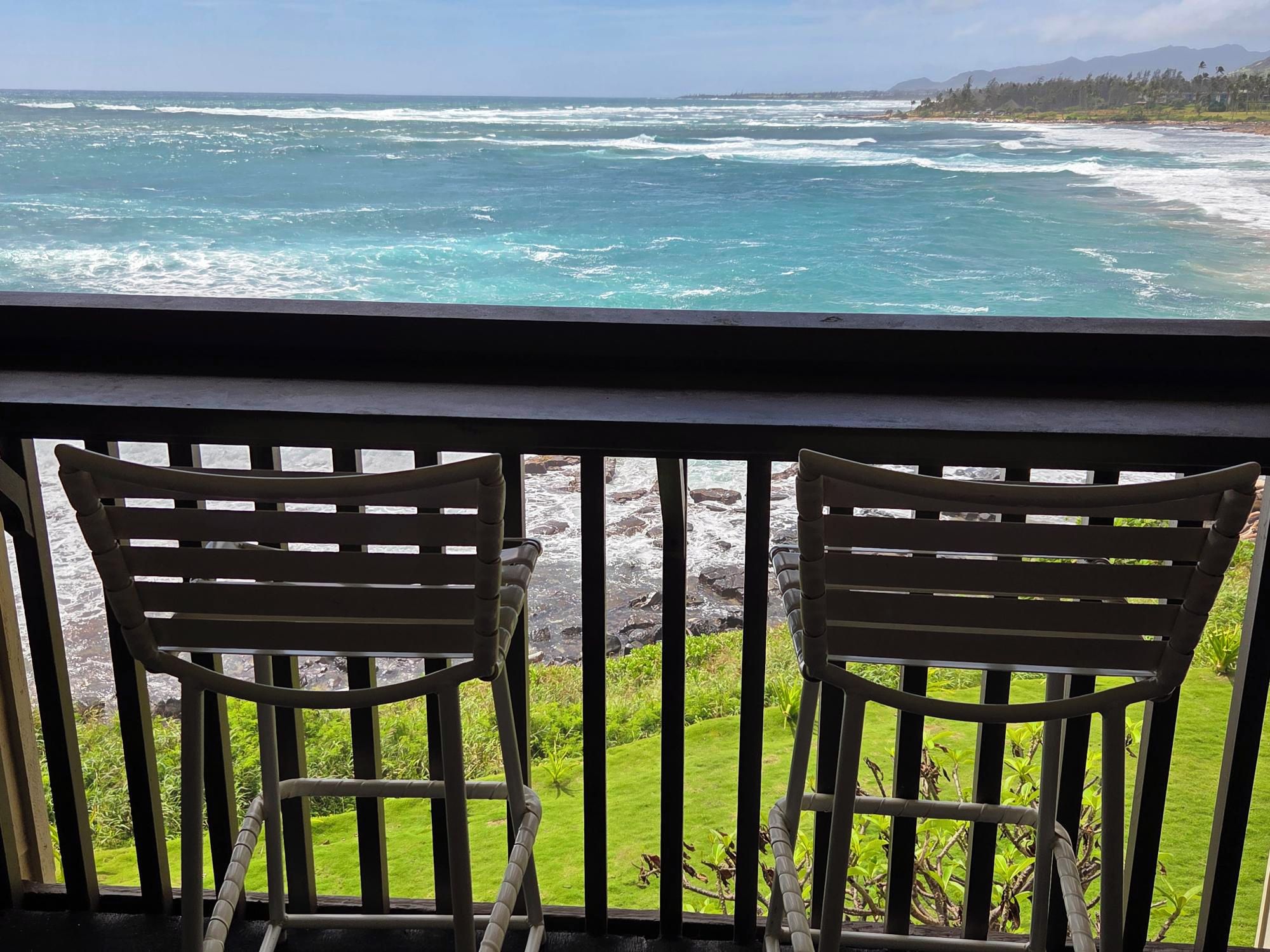 Two wooden chairs facing a rocky shoreline with ocean waves.