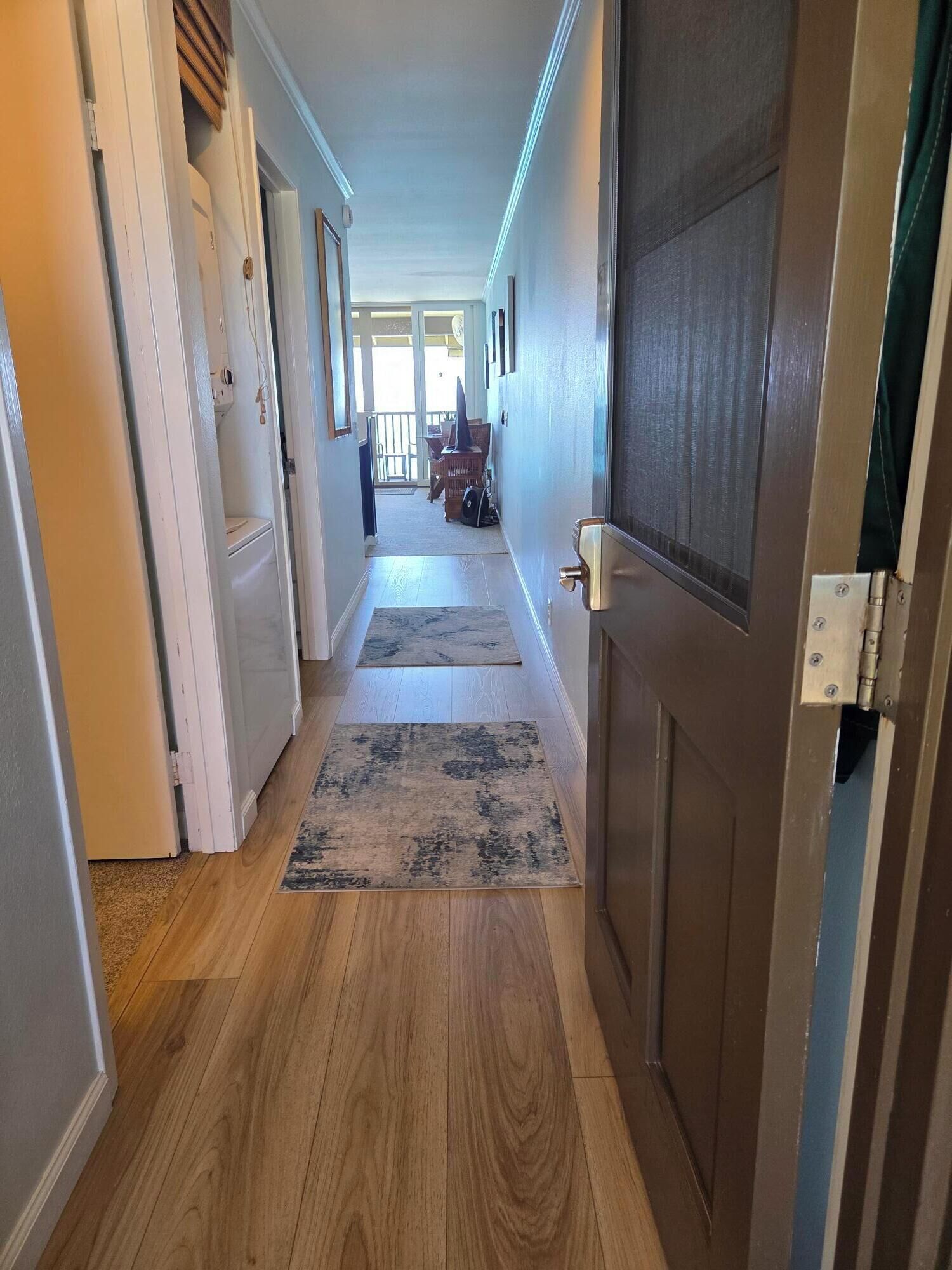 A hallway with wooden flooring, a closed door, and a view into a room with a table and chairs.
