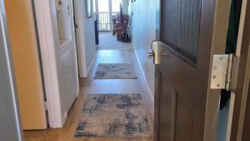 A hallway with wooden flooring, a closed door, and a view into a room with a table and chairs.