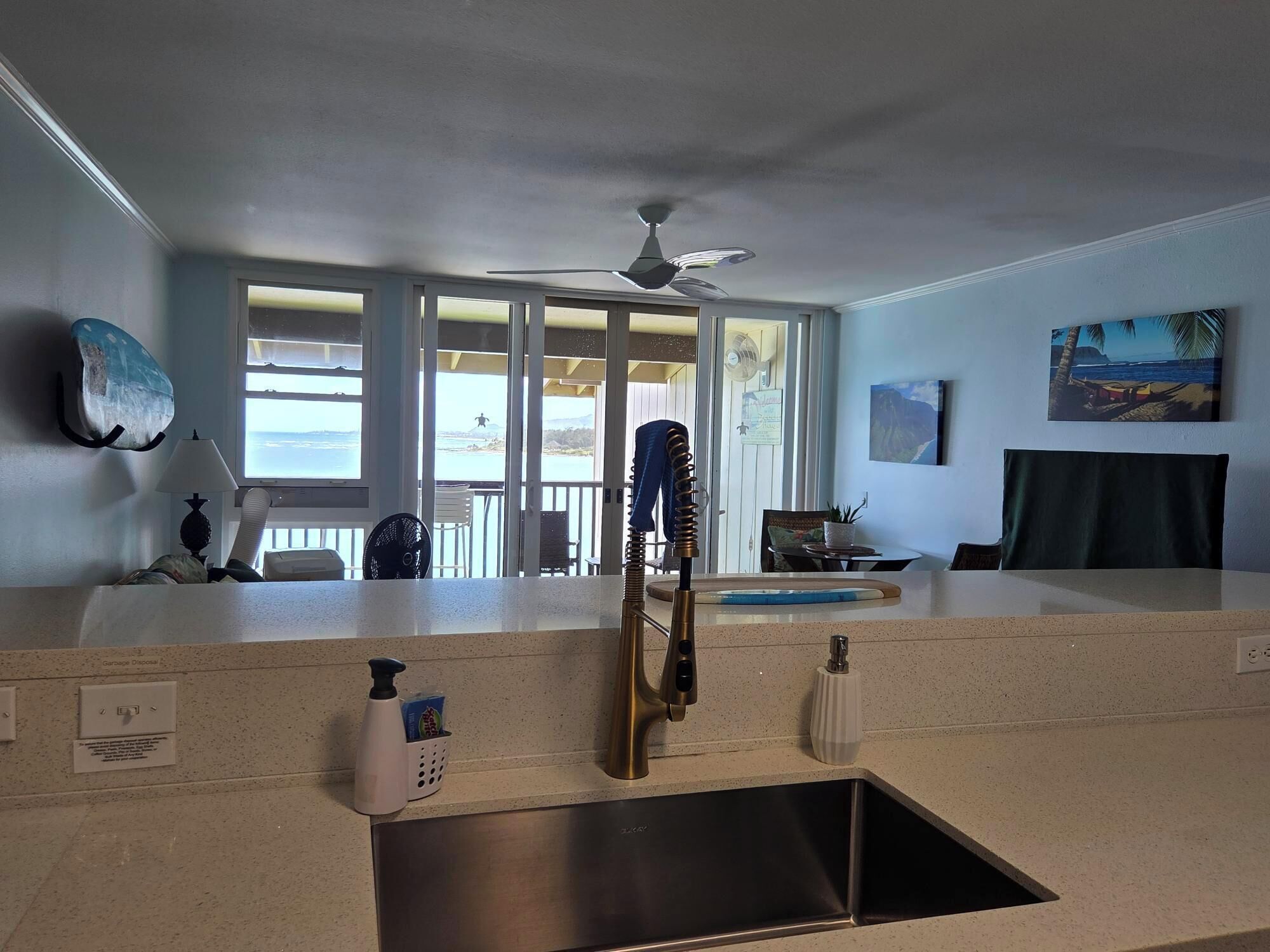 A kitchen with a stainless steel sink, a ceiling fan, and a view of the ocean through large windows.