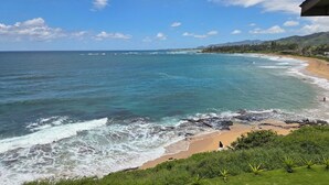 A coastal view with a beach, ocean waves, and a clear sky.