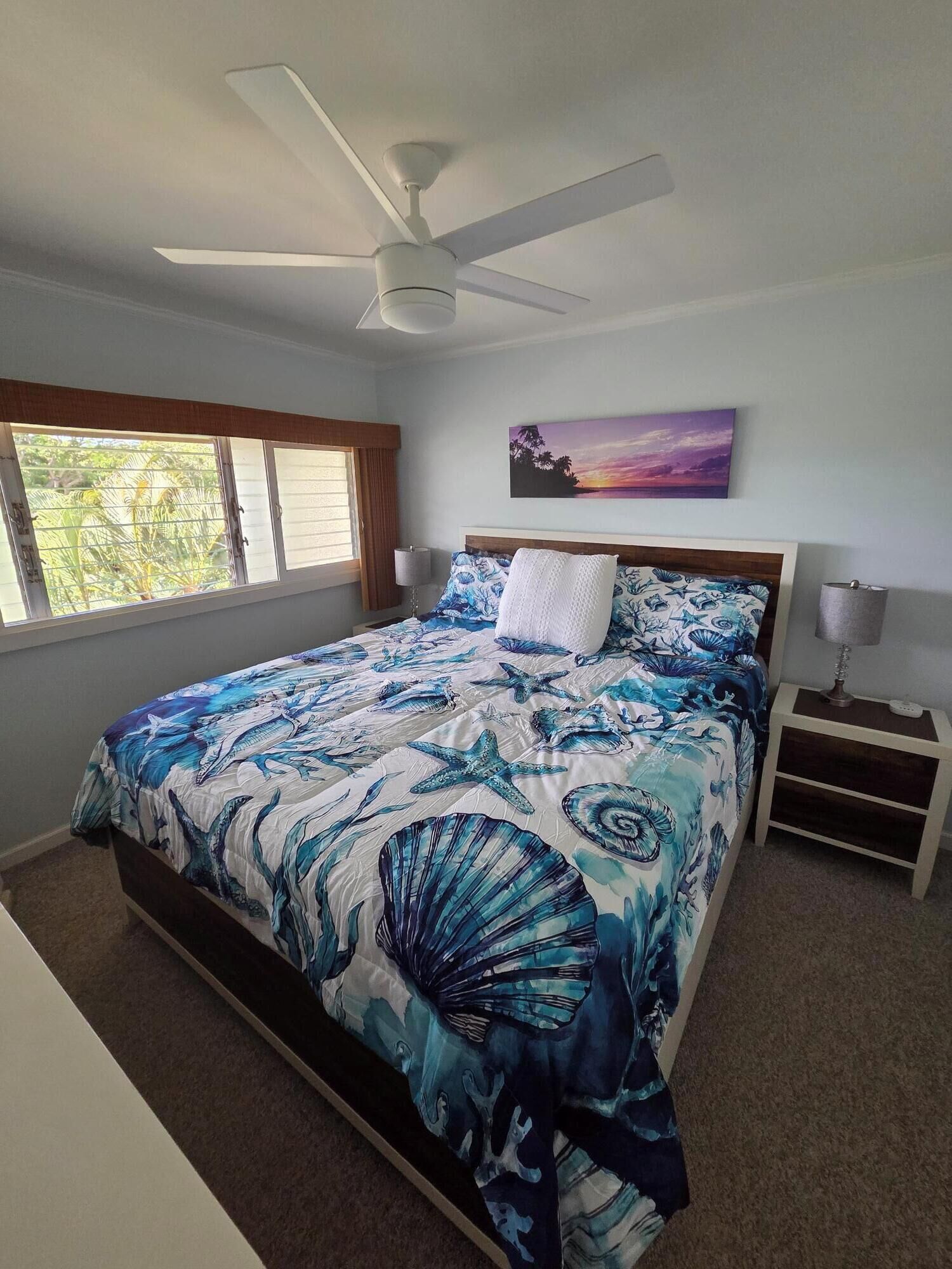 A bedroom with a bed, a ceiling fan, a nightstand, a lamp, and a painting on the wall.