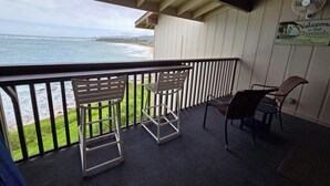A balcony with a view of the ocean, two chairs, a table, and a sign welcoming guests to the beach house.