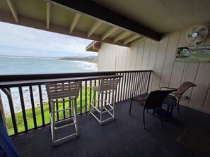 A balcony with a view of the ocean, two chairs, a table, and a sign welcoming guests to the beach house.