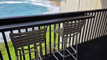 A balcony with two metal chairs, a view of the ocean, and a grassy area.