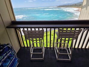 A balcony with two chairs facing a view of the ocean and a grassy area. - WOW! GORGEOUS TOP FLOOR DIRECT OCEANFRONT CONDO, TWO A/C UNITS, FREE PARKING! (Kapaʻa)