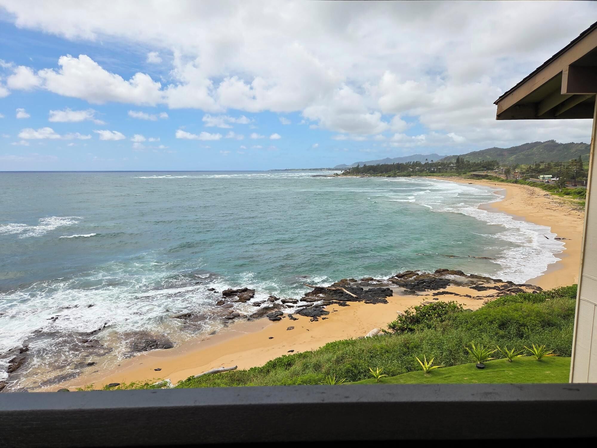 A beach with waves, a sandy shore, and a view of mountains in the distance.