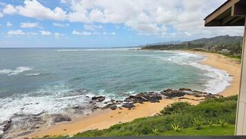 A beach with waves, a sandy shore, and a view of mountains in the distance.