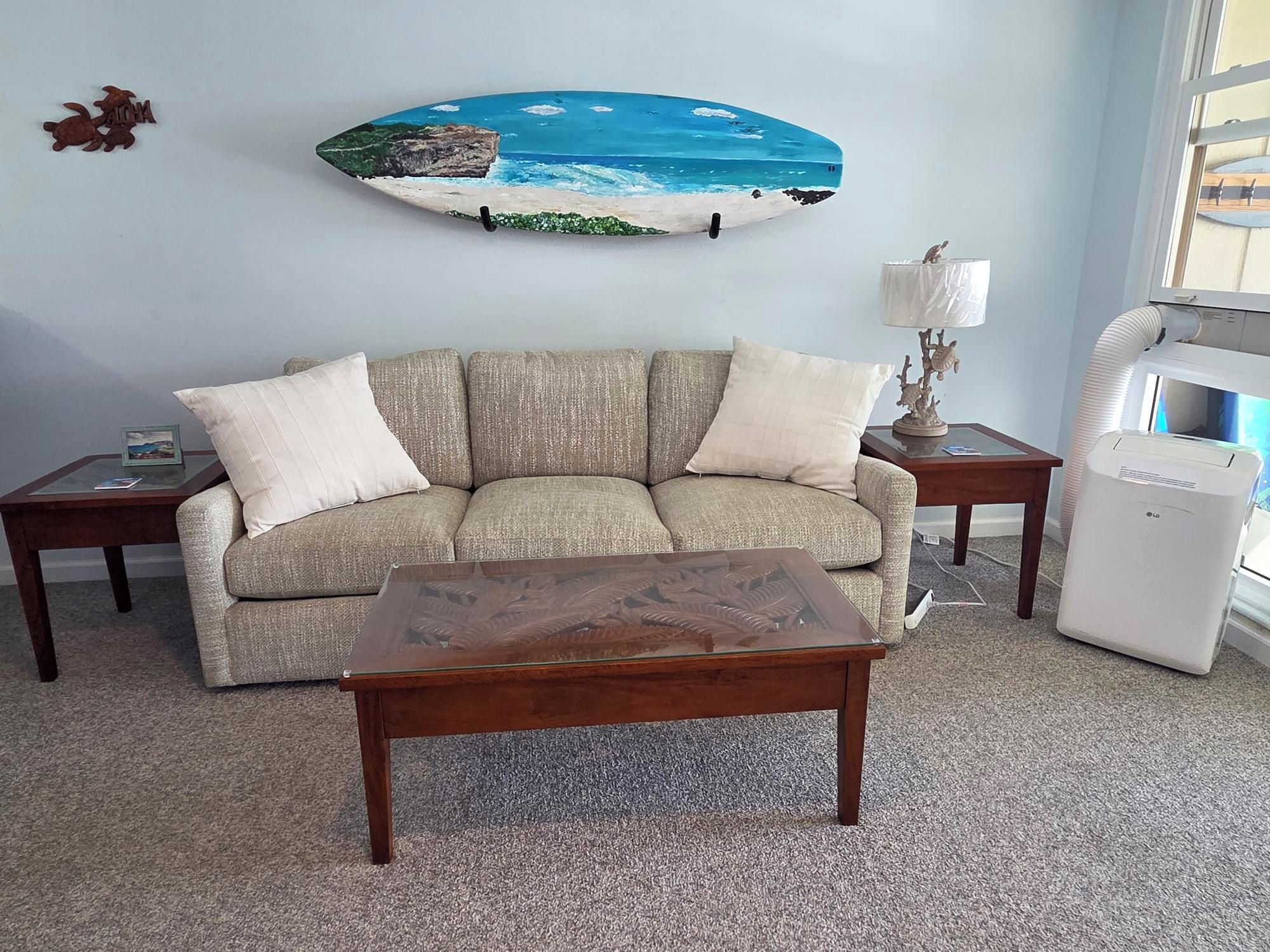 A living room with a sofa, a coffee table, a lamp, and a wall-mounted surfboard decoration.
