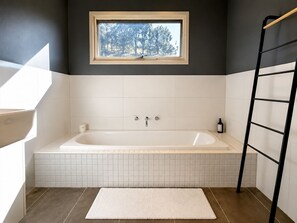 A bathroom with a bathtub, a window with a view of trees, and a black ladder. - Moonrise by Ready Set Stay (Harcourt North)