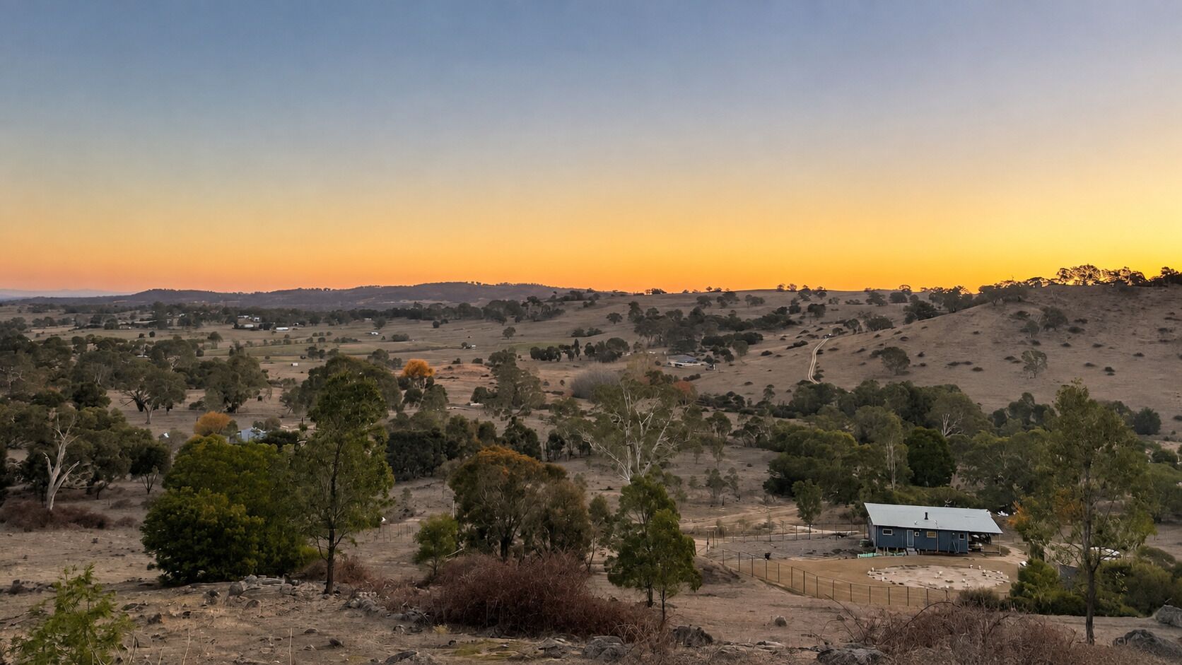 A rural landscape with a small house surrounded by trees and open fields.