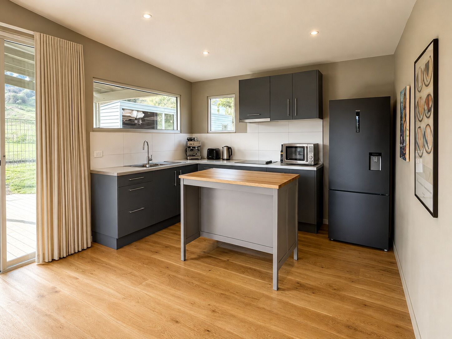 A modern kitchen with a central island, dark cabinetry, and a stainless steel refrigerator.
