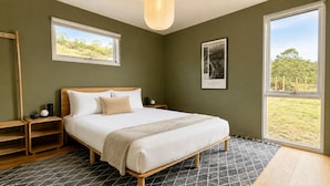 Quarto com cama, mesas de cabeceira, janela com vista e um quadro na parede.