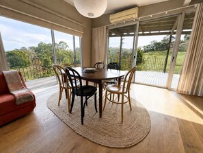 A dining area with a round table, chairs, a red sofa, and a view of a garden through large windows. - Moonrise by Ready Set Stay (Harcourt North)