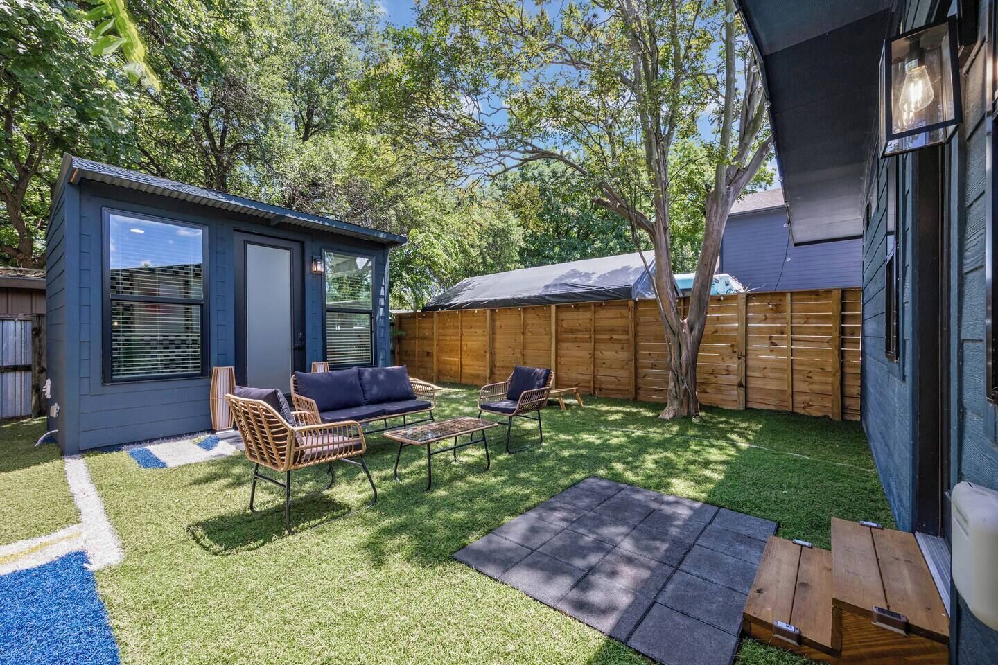 Un patio trasero con una pequeña estructura azul, muebles de exterior y una valla de madera.