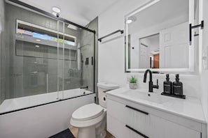 Ein modernes Badezimmer mit einer gläsernen Dusche, einer weißen Toilette, einem Waschbecken mit Spiegel und zwei Seifenspendern.