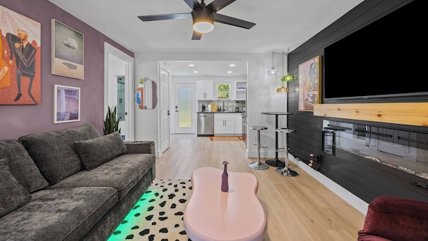 Una sala moderna con un sofá gris, un reposapiés rosa y un ventilador de techo.