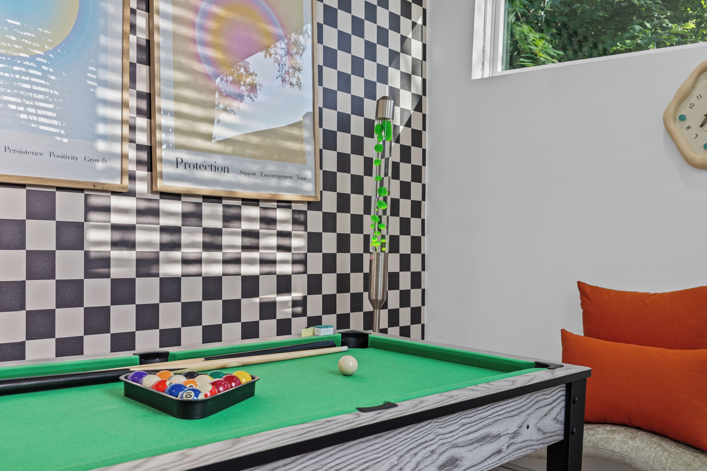 A pool table with balls, a cue stick, and a framed picture on the wall.