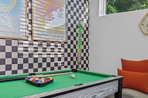 A pool table with balls, a cue stick, and a framed picture on the wall.